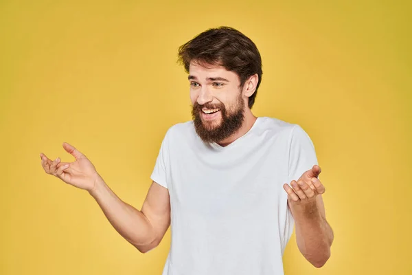 Barbudo hombre blanco camiseta emociones gestos con las manos divertido fondo amarillo — Foto de Stock