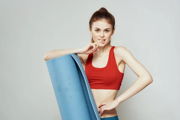 Vrouw houdt in de hand een mat voor fitness sport slanke figuur oefeningen lichte achtergrond — Stockfoto