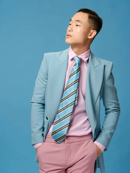 Handsome Asian guy in suit on a blue background straightens his jacket and pink trousers close-up cropped view
