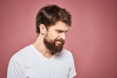 Beyaz tişörtlü duygusal sakallı adam hoşnutsuz pembe arka plan