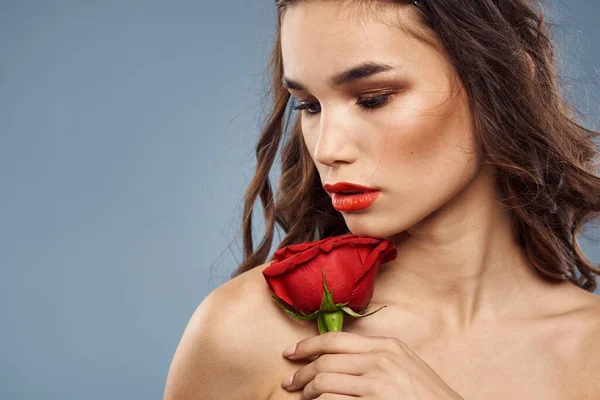 Portrait de femme avec rose rouge près du visage sur fond gris et maquillage cheveux bouclés — Photo