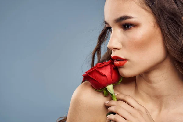 Portrait de femme avec rose rouge près du visage sur fond gris et maquillage cheveux bouclés — Photo