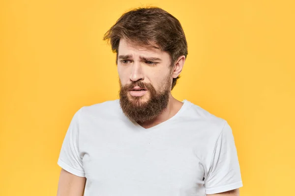 하얀 티셔츠를 입고 노란 배경을 가진 남자의 얼굴 표정을 하고 있는 수염 남자의 감정 — 스톡 사진
