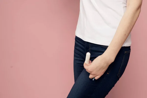 Mujer con un tampón en la mano días críticos higiene blanco camiseta jeans rosa fondo ciclo menstrual — Foto de Stock