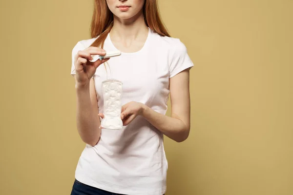 Meisje met een tampon en een pad in de hand op een beige achtergrond wit t-shirt bijgesneden uitzicht — Stockfoto