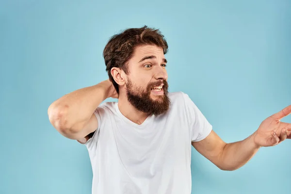 Hombre emocional con una barba en una camiseta blanca fondo azul estilo de vida divertido — Foto de Stock