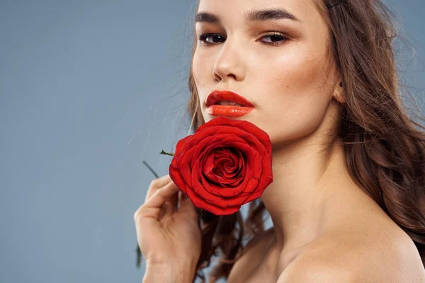 Portrait d'une femme avec une rose rouge dans les mains sur un fond gris épaules nues maquillage du soir — Photo