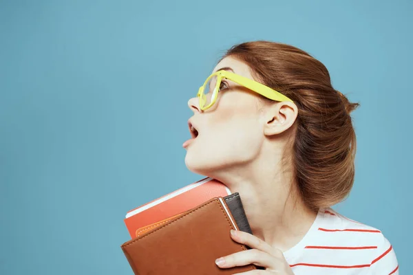 Красивая студентка с блокнотами и в желтых очках в синем учебном заведении — стоковое фото