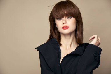 Güzel bir kadın şık giyiniyor. Çekici görünüyor. Bej bir arka planda gülüyor. 