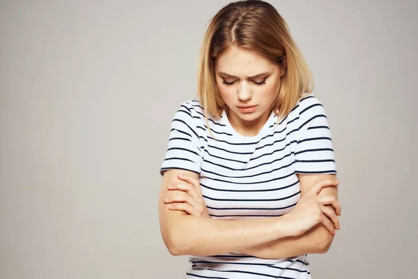 Een vrouw in een gestreept T-shirt houdt haar handen voor haar emoties onaangenaam licht achtergrond — Stockfoto