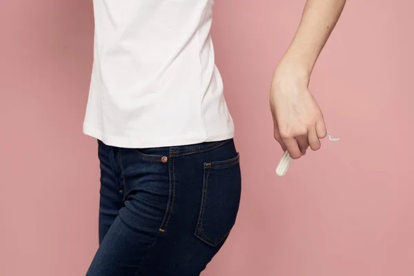 Frau mit einem Tampon in der Hand kritischen Tagen Hygiene weißes T-Shirt Jeans rosa Hintergrund Menstruationszyklus — Stockfoto