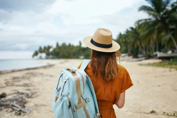 Um viajante com uma mochila azul em um chapéu e um vestido de verão caminha na praia — Fotografia de Stock