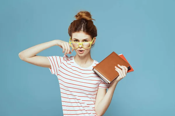 Estudante feminina com livros em mãos em um fundo azul e óculos amarelos modelo penteado corte vista — Fotografia de Stock