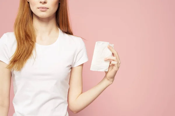 Piros hajú nő egy pad a kezében, és egy fehér póló egy rózsaszín háttér higiéniai ellátás a megjelenés — Stock Fotó