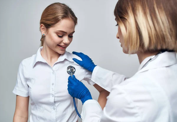 Mulher médica com um estetoscópio segura um paciente pelo ombro em um fundo leve — Fotografia de Stock