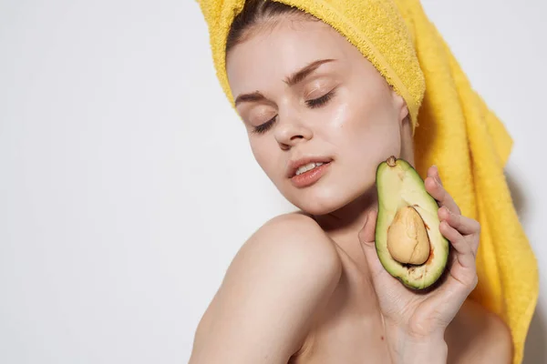 Mulher bonita com abacate nas mãos de uma toalha amarela na cabeça limpa a saúde da pele — Fotografia de Stock
