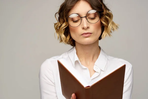 Mujer de negocios con bloc de notas y gafas sobre un fondo claro peinado éxito emociones —  Fotos de Stock