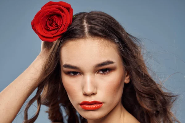 Portrait de femme avec rose rouge près du visage sur fond gris et maquillage cheveux bouclés — Photo