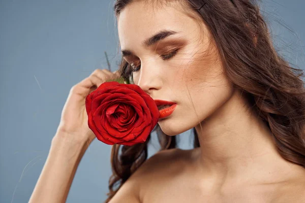 Retrato de una mujer con una rosa roja en sus manos sobre un fondo gris hombros desnudos maquillaje de noche — Foto de Stock