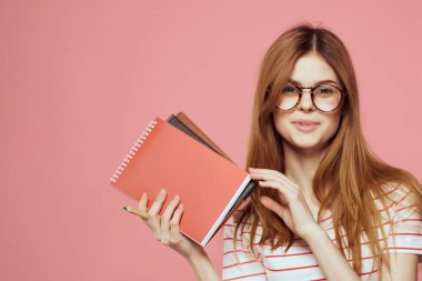 Elinde kitap tutan güzel bir kız öğrenci. El hareketleriyle el hareketi yapıyor. Pembe arka plan.