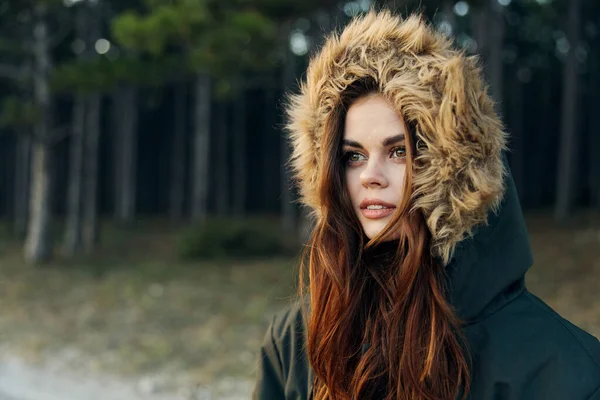 Mulher jaqueta turística quente com um capuz na natureza contra o fundo das árvores — Fotografia de Stock