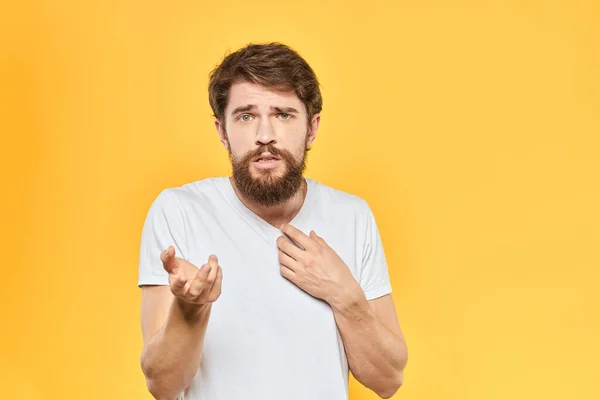 Бородатий чоловік в білій футболці жести з емоціями студії жовтого фону — стокове фото