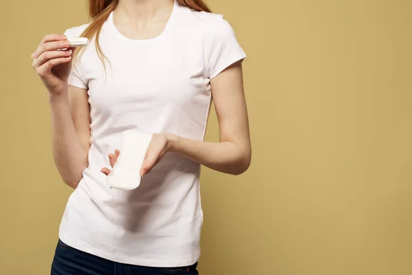 Κορίτσι με ένα ταμπόν και ένα μαξιλάρι στο χέρι της σε ένα μπεζ φόντο λευκό t-shirt περικοπή άποψη — Φωτογραφία Αρχείου