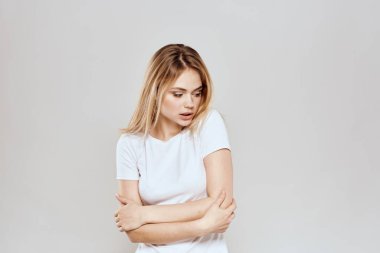 Beyaz tişörtlü neşeli sarışın. El hareketleriyle arka planını aydınlatıyor.