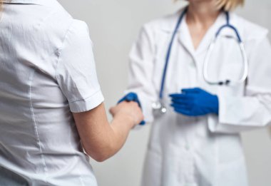 Hemşire, steteskopla mavi eldivenli ve hafif arka planda hastayla el sıkışıyor.