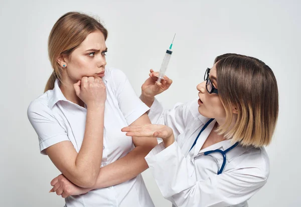 A nurse in a medical gown holds a syringe in her hand and a patient on a light background — Stock Photo, Image