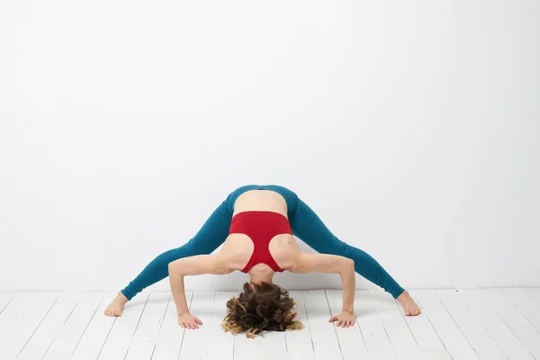 Wanita olahraga di ruang cerah melakukan yoga dalam pertumbuhan penuh legging biru dan atas tangki merah — Stok Foto