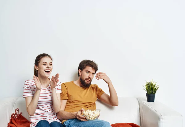 줄무늬 티셔츠를 입은 여자와 소파에 앉아 밝은 방에서 TV 를 보고 있는 남자 — 스톡 사진