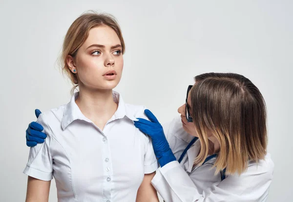 Una enfermera con guantes azules examina a un paciente con una camiseta blanca sobre un fondo claro — Foto de Stock