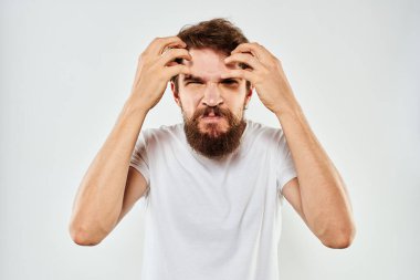 Beyaz tişörtlü duygusal sakallı adam elleri açık arka planda jestler yapıyor.