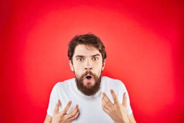 Duygusal sakallı adam elleri beyaz tişörtlü agresiflik, hoşnutsuzluk kırmızı arka planda hareket eder.