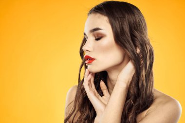 Çıplak omuzlu, kırmızı dudaklı, sarı arkaplanlı bir kadın.