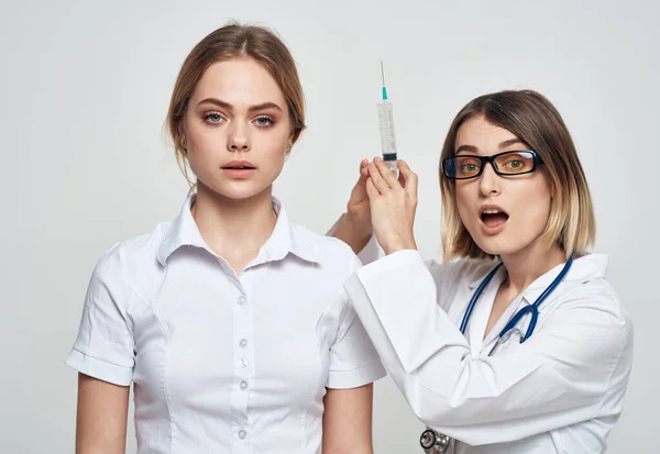 En sjuksköterska i medicinsk klänning håller en spruta i handen och en patient på en ljus bakgrund — Stockfoto