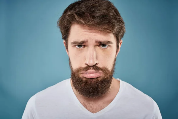 Bearded man displeased facial expression emotions close-up blue background white t-shirt