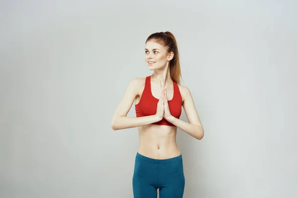 Una mujer con una camiseta roja sobre un fondo claro se dedica a gestos de fitness con las manos una figura delgada — Foto de Stock