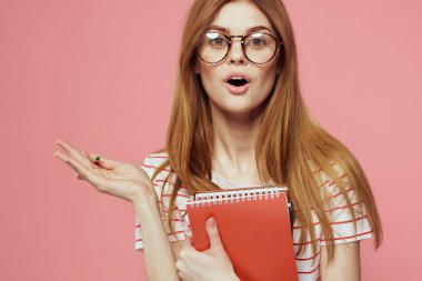 Elinde kitap tutan güzel bir kız öğrenci. El hareketleriyle el hareketi yapıyor. Pembe arka plan.