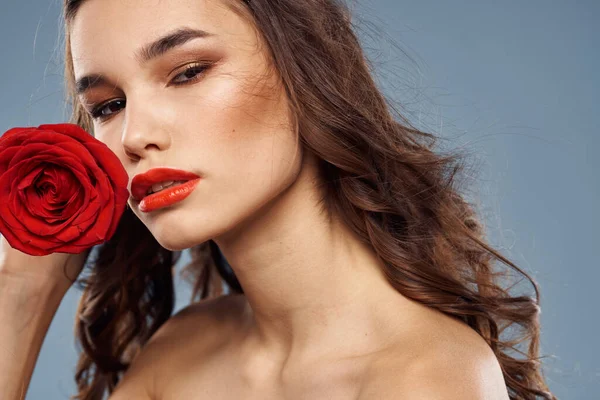 Retrato de una mujer con una rosa roja en sus manos sobre un fondo gris hombros desnudos maquillaje de noche — Foto de Stock