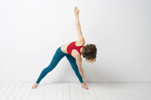 Mujer deportiva en una habitación luminosa haciendo yoga en leggins azules de pleno crecimiento y una camiseta roja —  Fotos de Stock