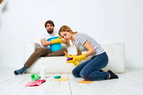 Woman washes the floors A man sits on the couch at home interior cleaning — Stock Photo, Image