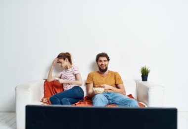 Bir adam ve bir kadın TV 'nin önündeki kanepede oturuyorlar ve yeşil bir çiçek evin içinde.