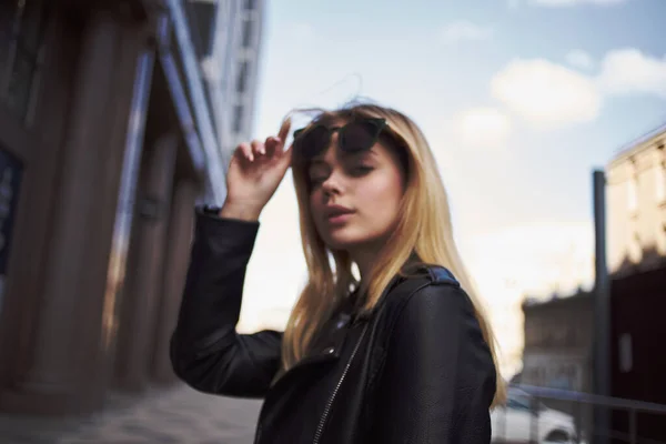 Mujer de moda en una chaqueta de cuero y gafas de sol cerca del edificio en la calle —  Fotos de Stock