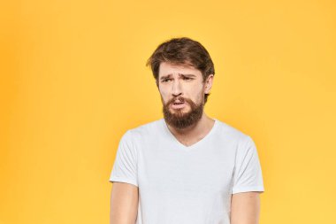 Sakallı adam duyguları, yüz ifadesi, beyaz tişört, sarı arka plan.