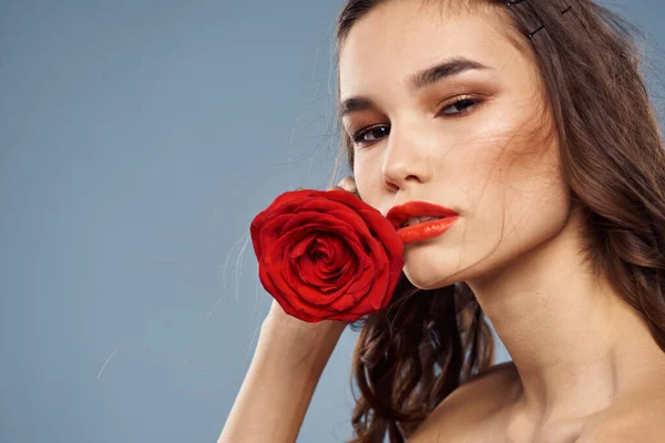 Portrait d'une femme avec une rose rouge dans les mains sur un fond gris épaules nues maquillage du soir — Photo