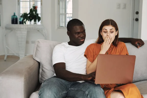 Un homme d'apparence africaine et une femme sur le canapé avec un ordinateur portable regardant le moniteur — Photo