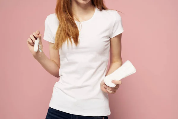 Vrouw met een kussen in haar hand op een roze achtergrond jeans T-shirt tampons hygiëne frequentie — Stockfoto