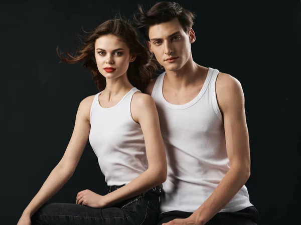 Hommes et femmes amoureux dans des T-shirts identiques sur un fond noir assis à côté — Photo